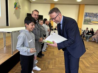 Landrat Alexander Tönnies überreicht einem lächelnden Jungen seine Einbürgerungsurkunde.